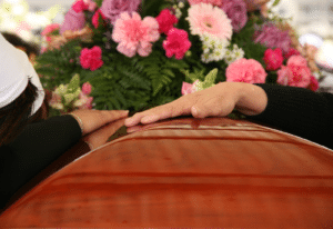 Image of two hands on a casket with flowers in the background