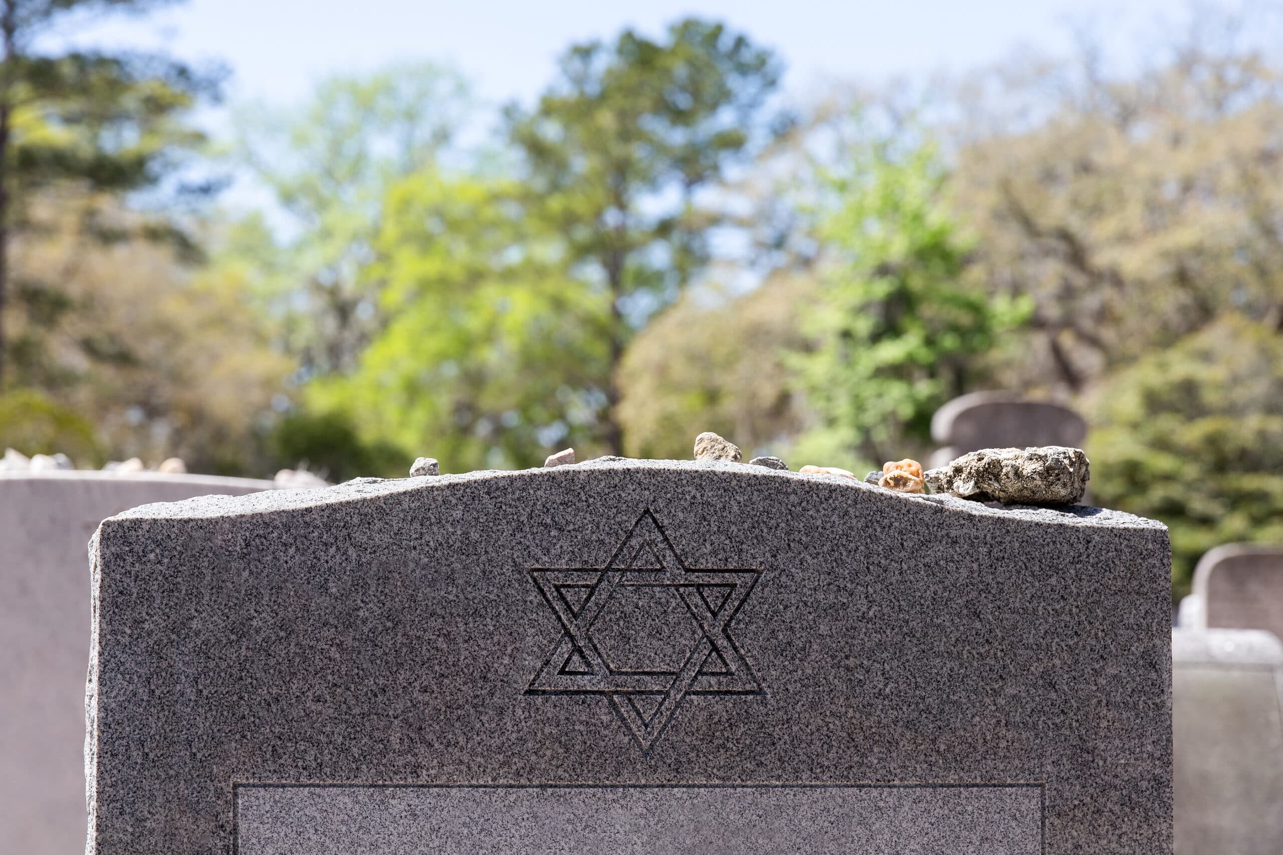 Headstone in a Jewish cemetery with Star of David and memory stones. Selective focus on the foreground.